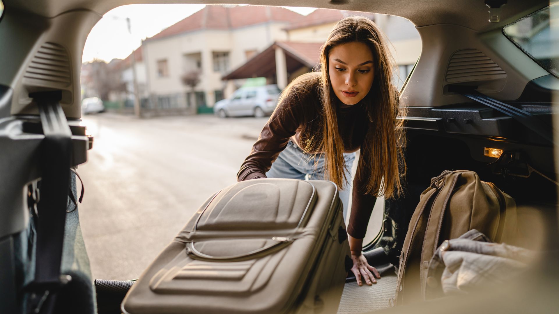 A woman leans into the trunk of a car to organize or retrieve a suitcase and backpack, possibly symbolizing a fresh start or major life transition such as moving out after a divorce in Nevada.