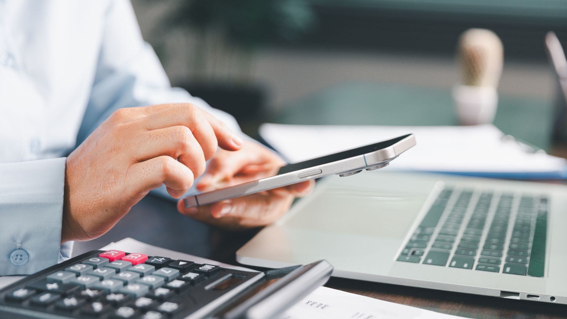 A close-up of a person using a tablet at a desk, with a calculator, laptop, and financial documents nearby—suggesting they are reviewing debts or assets, possibly related to managing an insolvent estate.