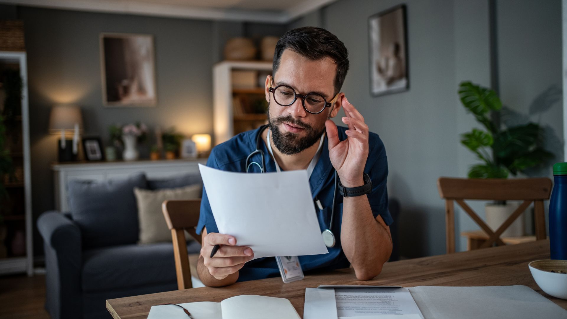 A healthcare professional sits at a table in a home setting, reviewing medical documents with a thoughtful expression—illustrating the careful planning and attention often needed when managing care for someone living with Alzheimer’s Disease.